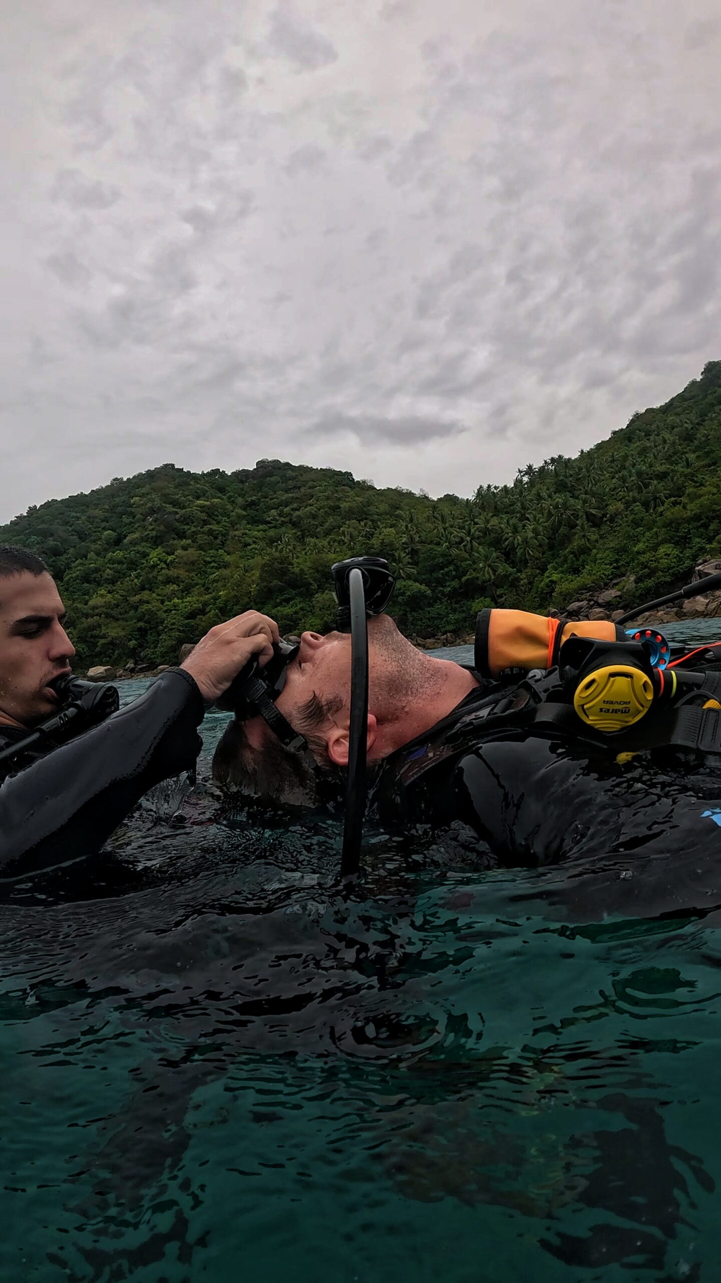Two Rescue Diver students in Koh Tao practicing surface rescue techniques, including airway management and equipment removal during scuba training.