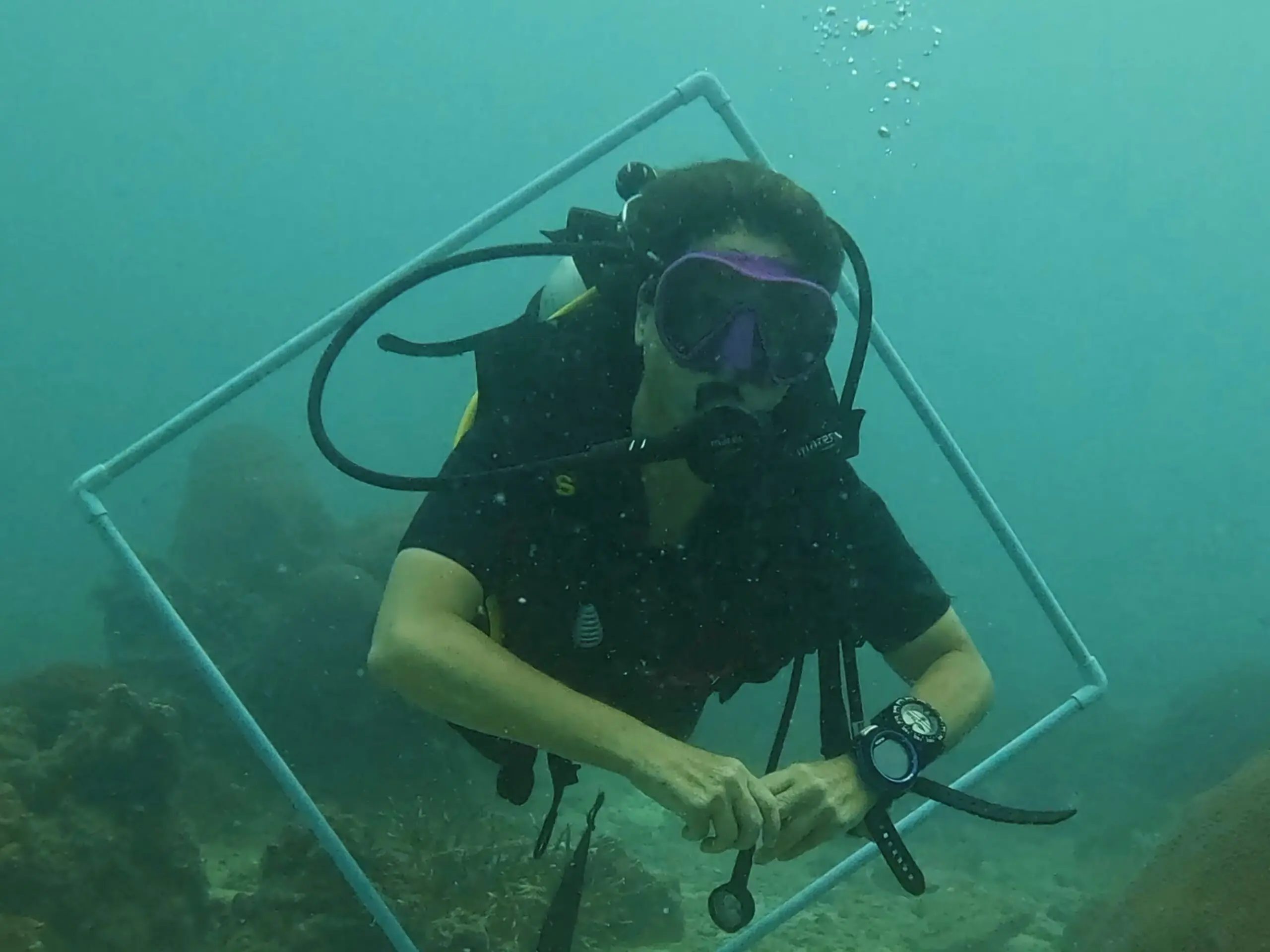Scuba diver practicing buoyancy control by swimming through an underwater frame during a training dive at Dive In Koh Tao.