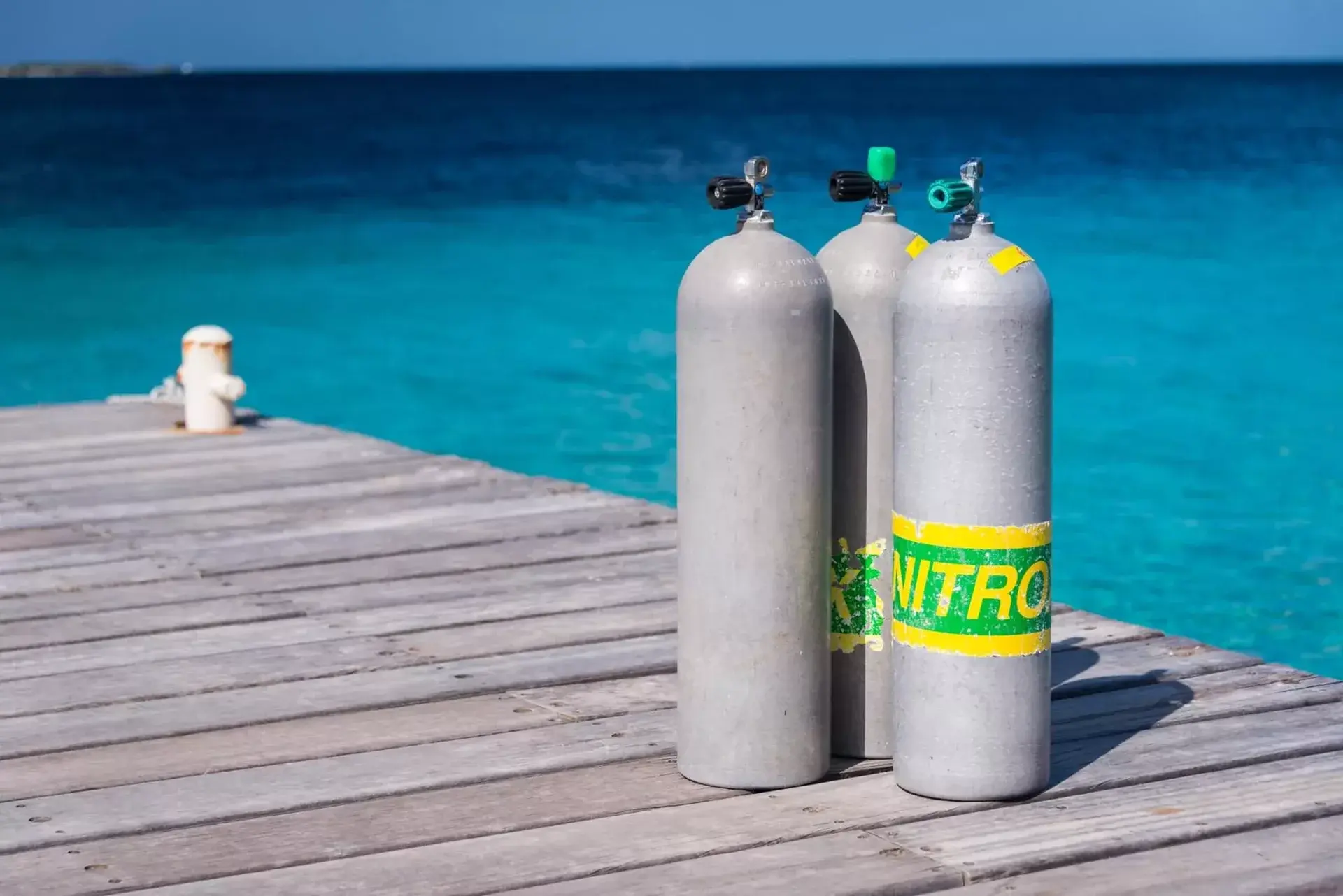Nitrox scuba tanks on a wooden pier overlooking the crystal-clear waters of Koh Tao, Thailand, ready for an SSI Enriched Air Nitrox dive.