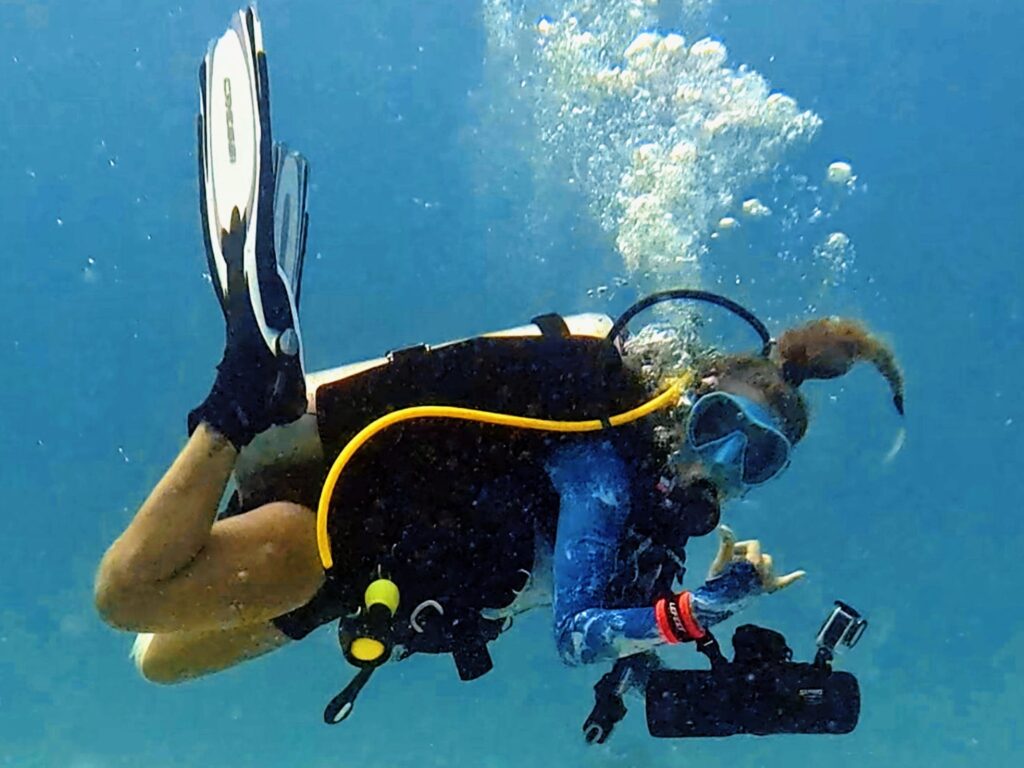Scuba diver giving a shaka hand sign while cruising with a DPV underwater scooter during a specialty dive training in Koh Tao, Thailand.