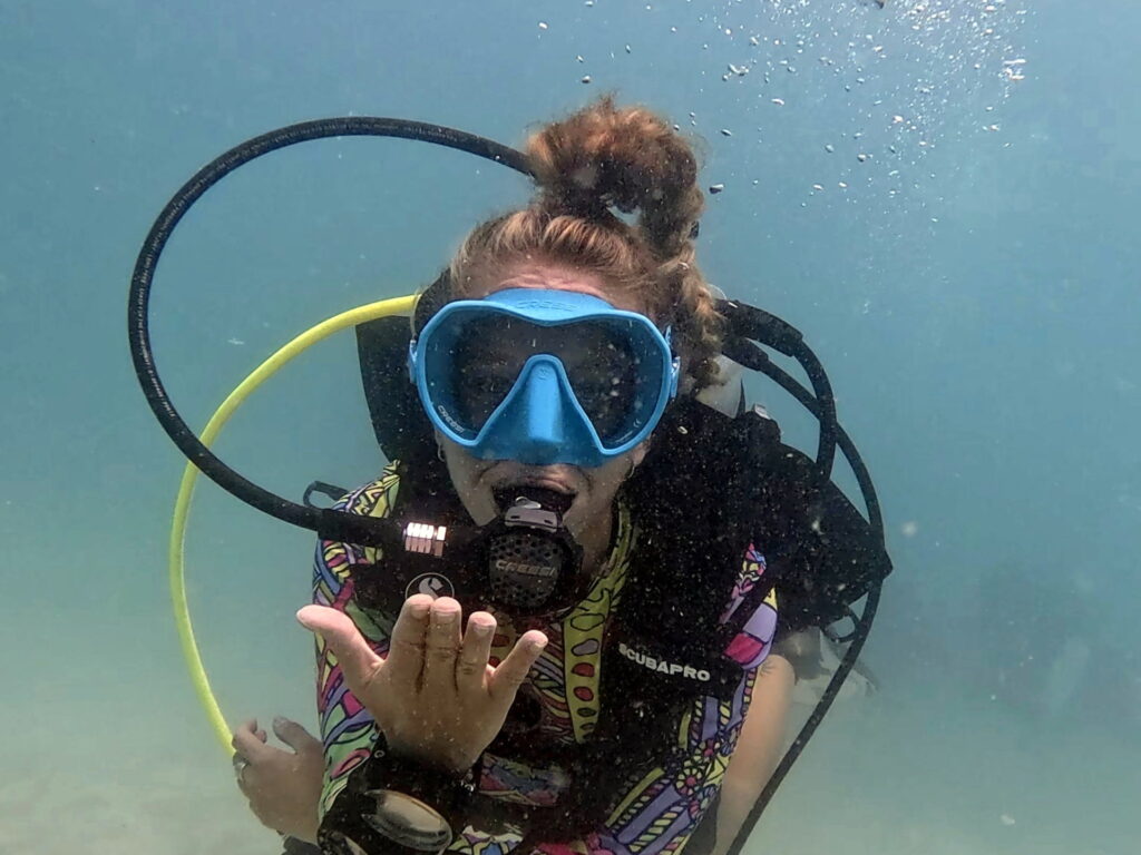 Scuba Diver Blowing a Kiss Underwater – Fun Dive in Koh Tao Scuba diver blowing a kiss underwater during a fun dive in Koh Tao, wearing colorful gear and a blue mask.