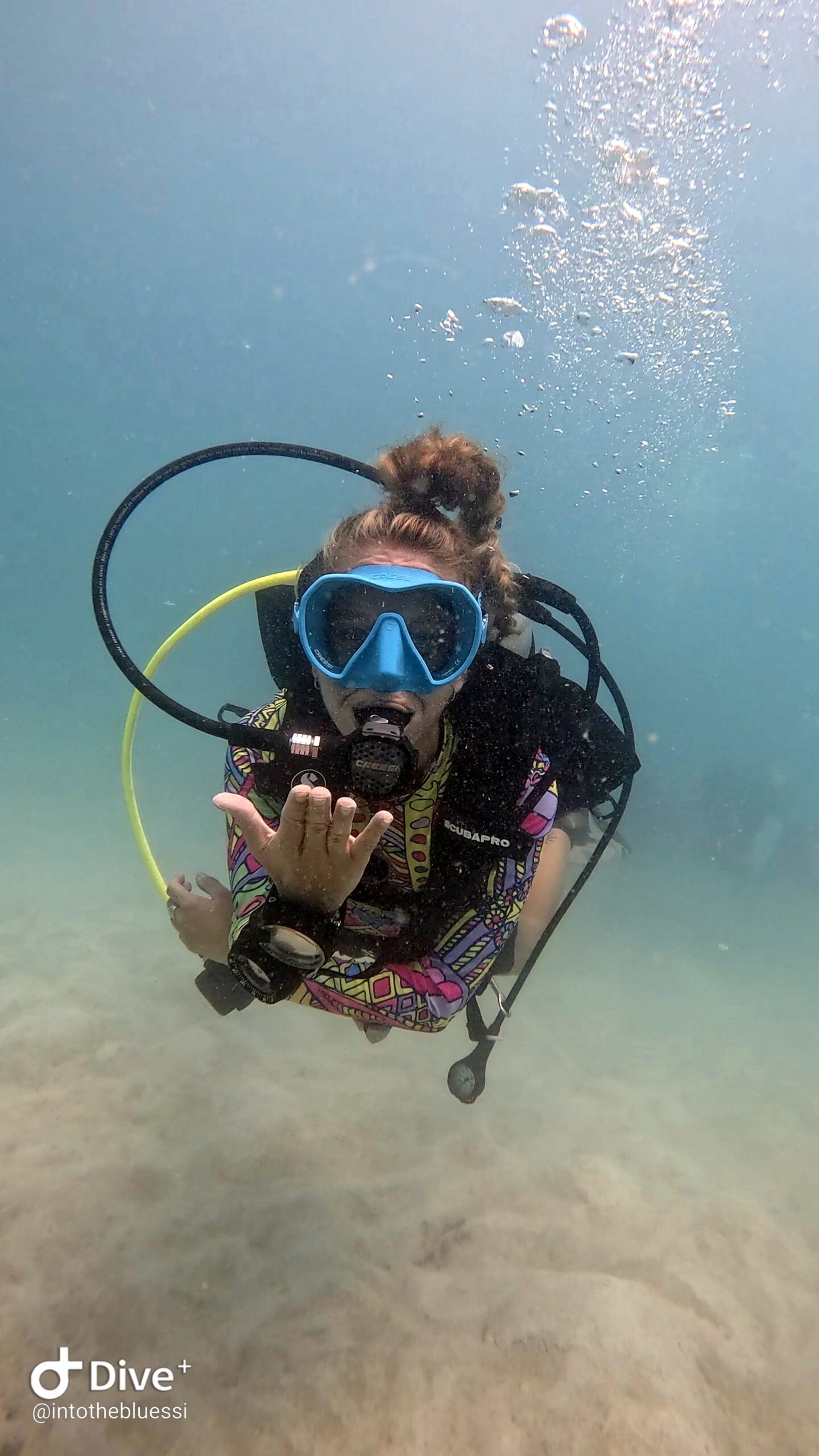 Scuba diver blowing a kiss underwater during a fun dive in Koh Tao, wearing colorful gear and a blue mask.