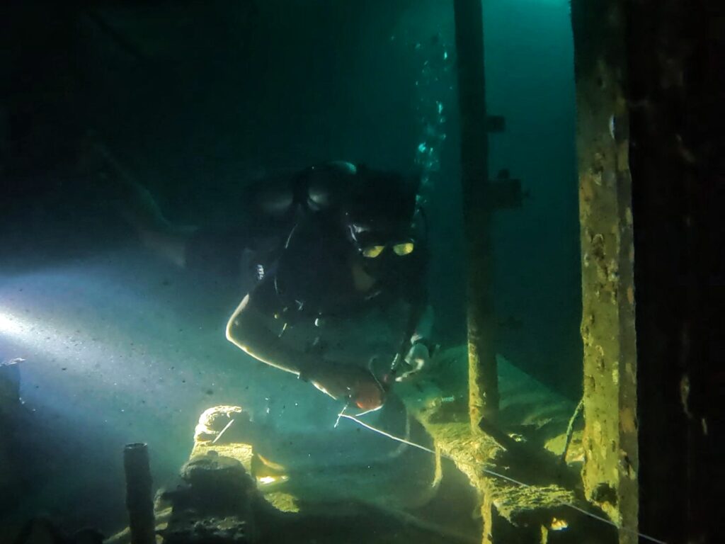 Scuba diving student disassembling a guideline reel inside a shipwreck during Advanced Wreck Diving Specialty training in Koh Tao.
