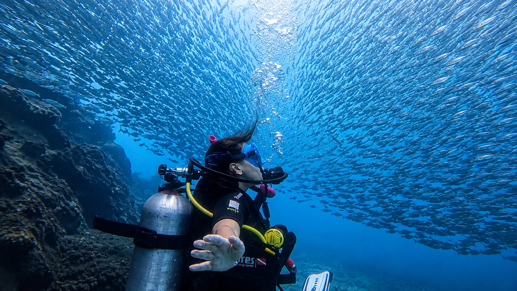 Scuba diver surrounded by a large school of fish while diving in the clear blue waters of Koh Tao, Thailand.