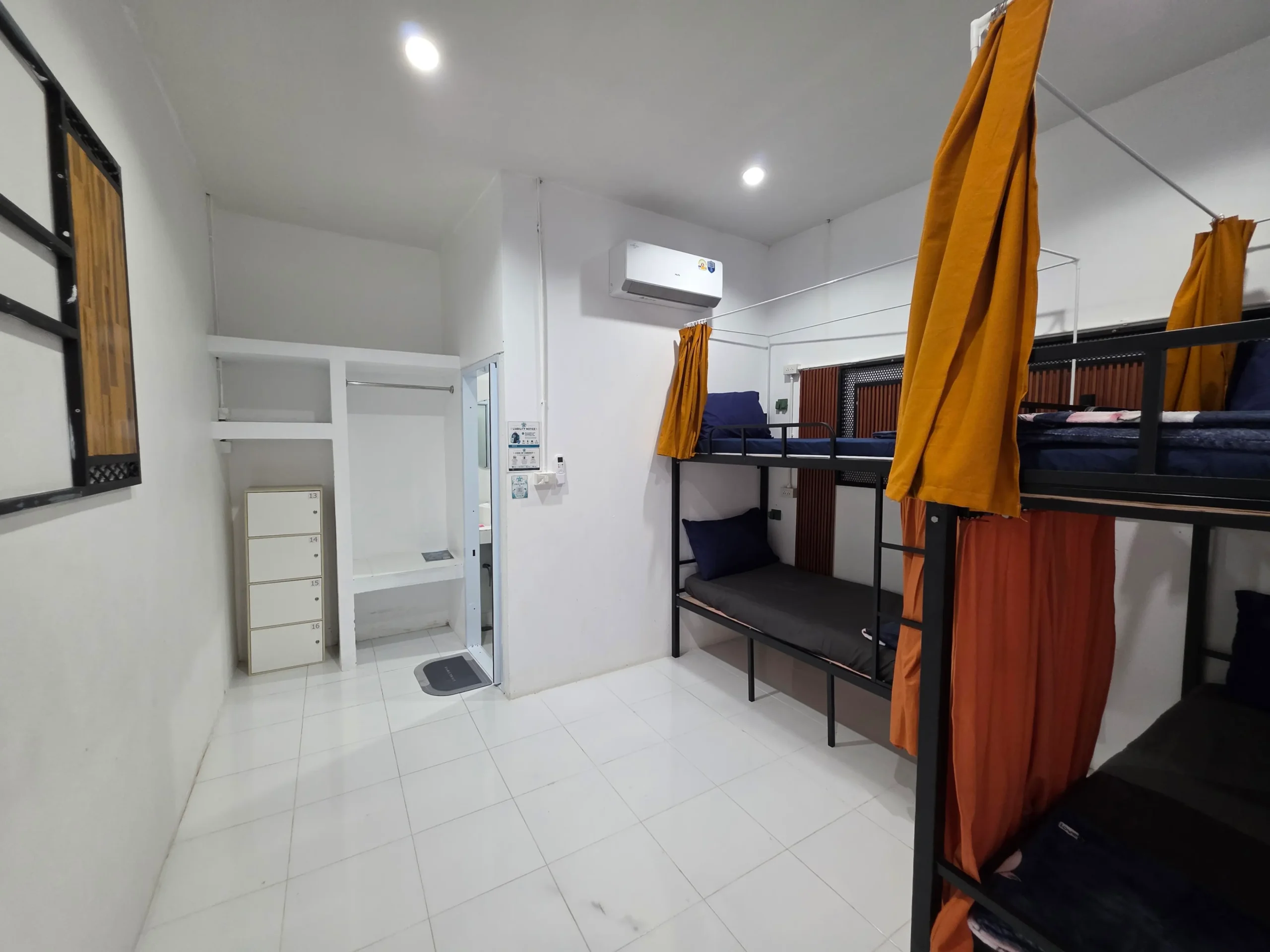 Hostel bunk beds with orange privacy curtains and air conditioning in Koh Tao, Thailand