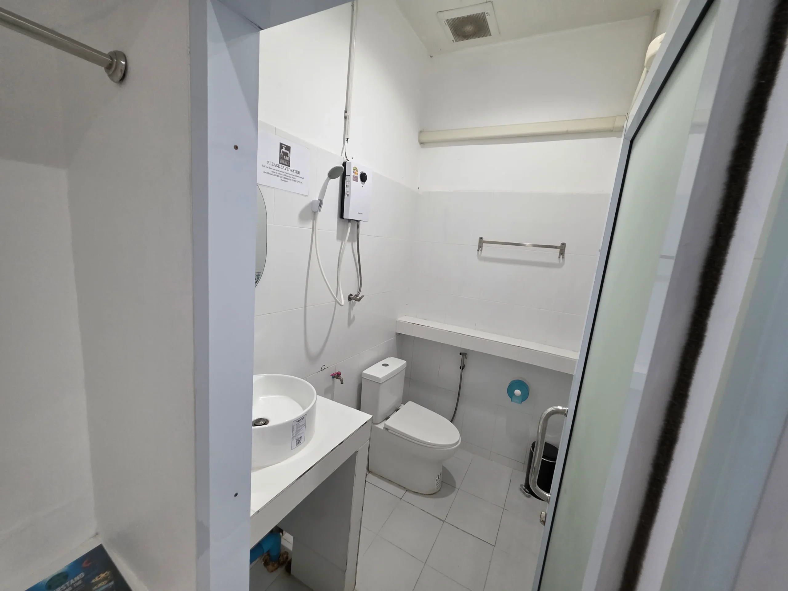 Clean tiled bathroom with a toilet, sink, handheld shower, water heater, and towel rail.
