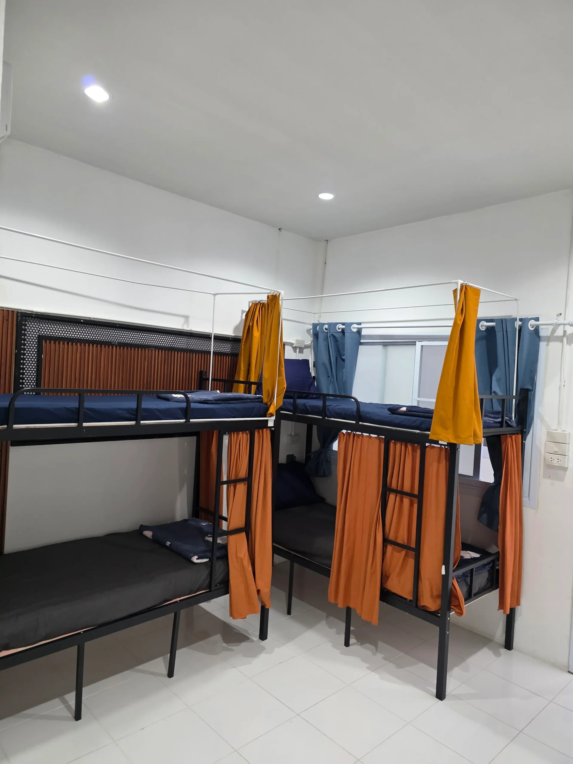 Dormitory room with bunk beds, dark blue mattresses, and orange privacy curtains.